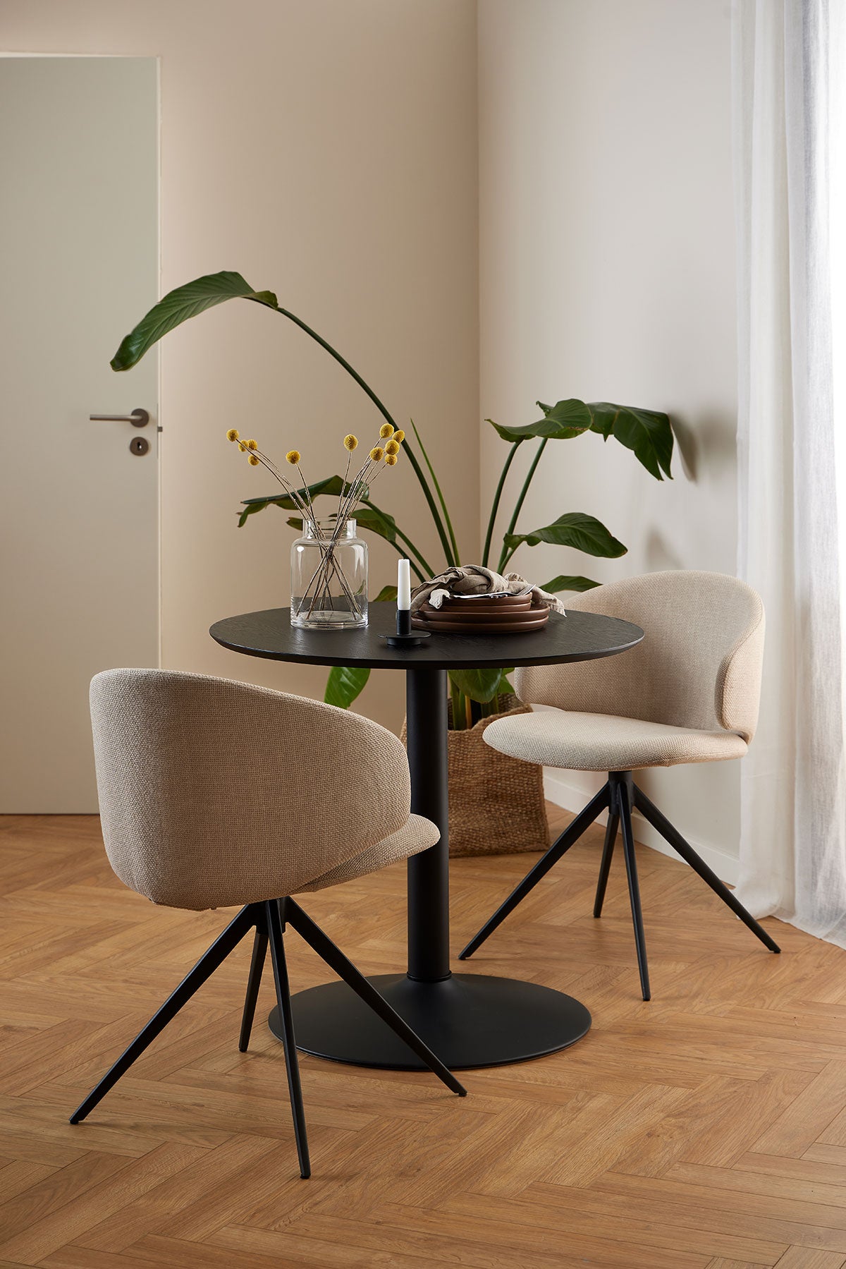 Ibiza Cafébord med to armstole i beige stof. Cafébordet er dekoreret med porcelæn, en lysestage og en vase.