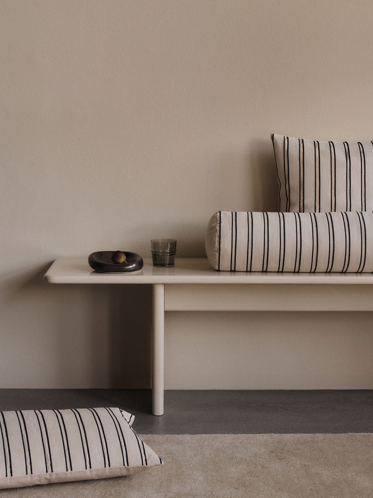 Bellure Skål i farven Rustic Bronze, som står på en bænk dekoreret med stribede pyntepuder