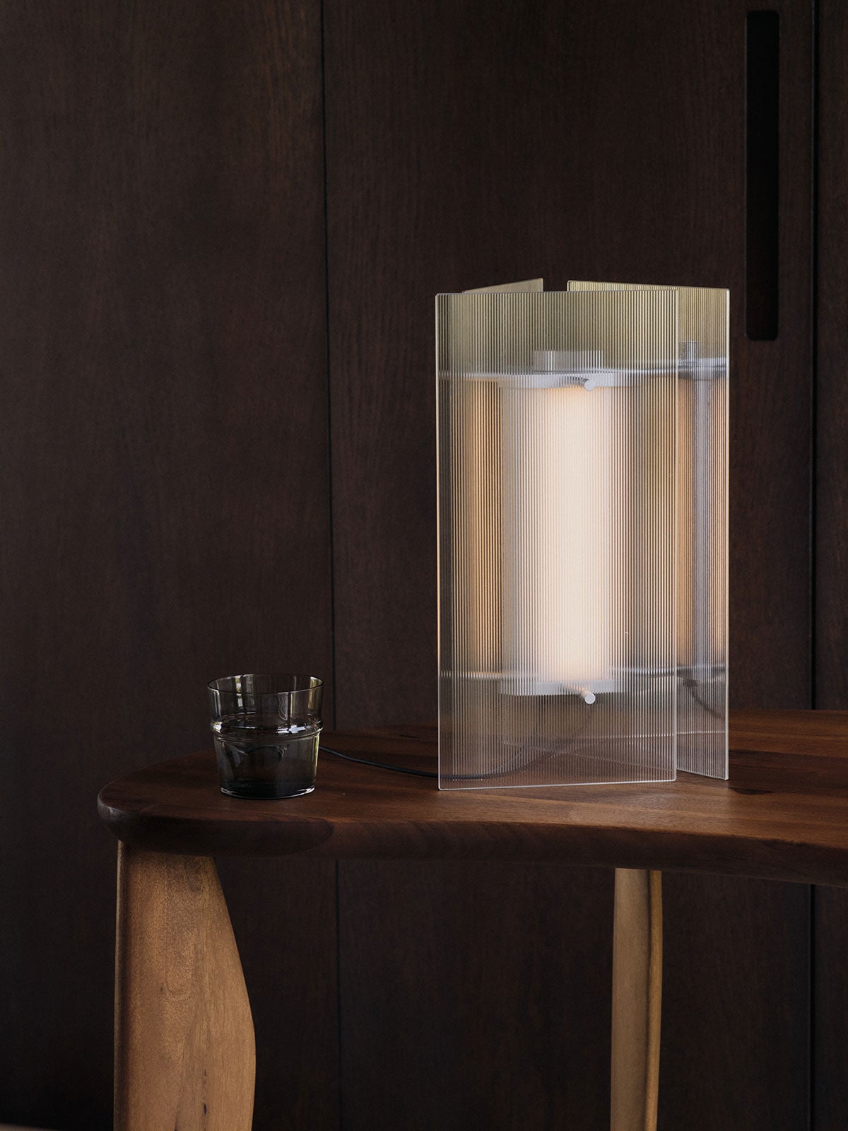 Oeste Bordlampe i glas, som står på et bord med et drikkeglas