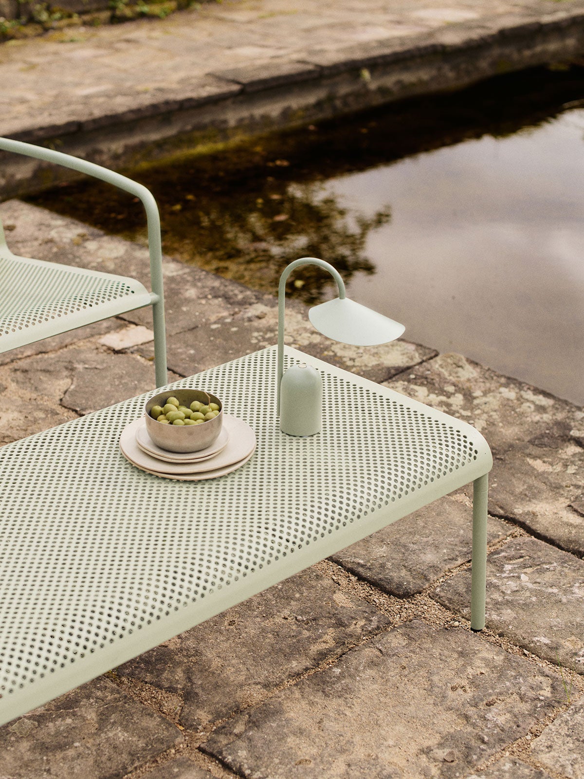 Dapple Loungebord 114x57 i farven Tea Green dekoreret med en bærbar lampe og en skål med oliven